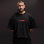 Uomo con T shirt nera oversize TAF The Art of Fighting e logo arancione sul petto fotografato su sfondo scuro
